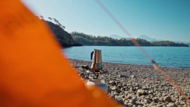 Türkiye 'de Akdeniz kıyısındaki boş çakıl taşı plajında, gaz ocağının üzerinde turuncu çadır ve kahve demliği. Vahşi doğa ve dijital detoks. Deniz kıyısında açık havada kahve yapmak. Denize odaklan