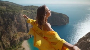 Yandan bakan mutlu gezgin özgürlüğü, açık kollarla kadını güldürüyor ve dağ manzarasından zevk alıyor, Türkiye 'nin Kelebek Vadisi' nde yaz tatili. Kız denizin üzerinde uçurumun tepesinde duruyor