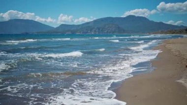waving sea with waves at sunny summer windy day at beautiful sandy empty beach Iztuzu in Turkey. beautiful mountain range on background