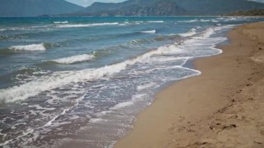 Türkiye 'nin güzel, kumlu, boş plajı Iztuzu' da güneşli yaz rüzgarlı bir günde dalgalarla dalgalanan denizi kapatın. Arka planda güzel dağ sıraları