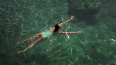 Akdeniz 'in berrak turkuaz sularında yüzen yeşil mayo giymiş seksi ve çarpıcı kadının yavaş çekim üst görüntüsü. tatil ve sağlık, Yaz Sezonu Fethiye, Türkiye