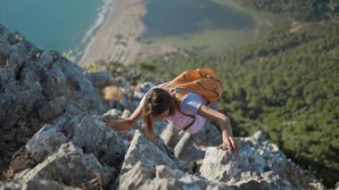 Teammate helping hiker to reach summit . Couple hiking in Turkey, helping hand concept. slow motion woman hiker rock climber climbs up on cliff on mountain over beautiful sea beach Iztuzu in Turkey