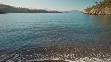 vertical panoramic filming of beautiful calm turquoise sea water at wild solitary pebble beach with cliffs at coast of mediterranean sea in Turkey. summer vacation, tourism and nature beauty