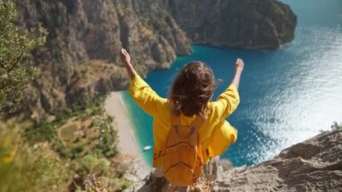 rear view happy traveler freedom filling woman with open arms smiling and enjoying mountains view, summer journey vacation in Butterfly valley,Turkey. girl stands on top of cliff over sea