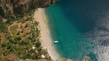 Türkiye 'nin Fethiye ilçesinde Kelebek Vadisi olarak bilinen Akdeniz kıyısında, turistler güneşli bir yaz gününde turkuaz mavi tropikal su boyunca yürürken geniş bir kırsal sahil havası.