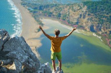 Dağın tepesinde yürüyücü vadi manzarasının keyfini çıkarıyor, kolları havada uçurumun kenarında duruyor. Iztuzu Plajı, Türkiye 'nin Dalyan Tepesi