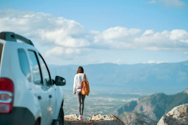 Rear view woman traveler enjoying mountain landscape, reaching summit destination on road trip