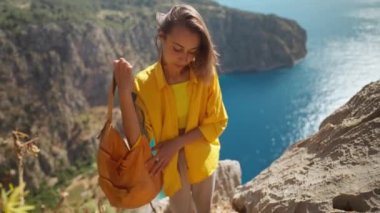 Outdoor portrait of happy smiling girl hiker climbing up on cliff and holding helping hand for reaching to summit cliff over sea. Active lifestyle adventure concept, Butterfly Valley, Turkey