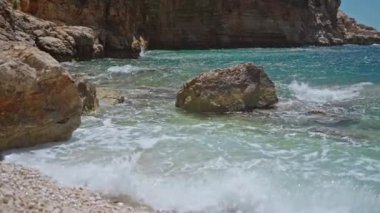slow motion sea waves crashing and foaming against rocky pebble beach on mediterranean sea shore. golden rocks coast meeting deep blue ocean water. Summer Tourism in Turkey concept
