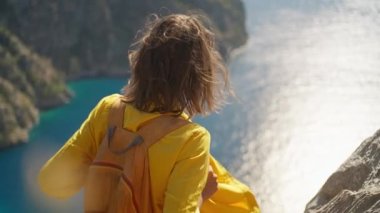 slow motion woman tourist with blowing hair enjoying sea coast view from high cliff over bay, summer journey vacation in Butterfly valley,Turkey. girl stands on top of cliff. go everywhere concept