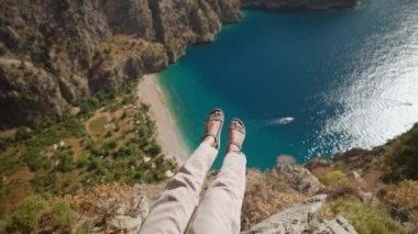 POV first person view of womans legs over beautiful Butterfly Valley bay and beach in Turkey. girl tourist hiker sits on cliff edge at popular touristic place, enjoying amazing view. go everywhere