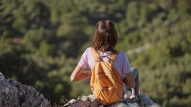 rear view girl hiker sits on edge of high cliff enjoying beautiful seascape of Aegean coastline mediterranean sea in Turkey from high mountain. Summer vacation and travel in Turkey. go everywhere