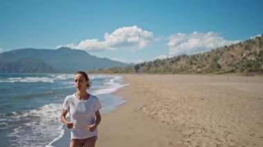 Sporty woman running ocean beach. Young caucasian female exercising outdoors running seashore. Concept of healthy running and outdoors exercise. Active, sporty athlete jogging. Summer active