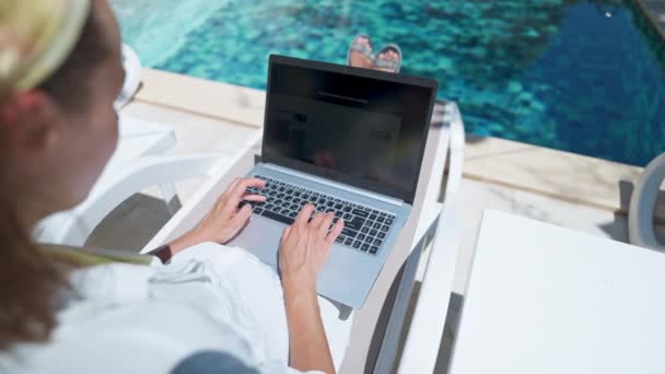 リゾートホテルのプールでサンラウンジャーに横たわっている間 ラップトップコンピュータオンラインインターネットを使用して顔のない女性 — ストック動画