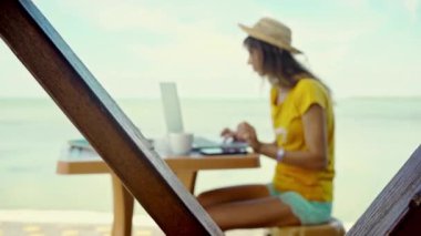 Şapkalı, akıllı telefonlu, deniz kenarında dizüstü bilgisayarda çalışan serbest çalışan bir kadın portresi. Özgürlük, uzak iş, serbest çalışma, seyahat ve tatil kavramları