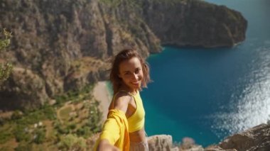 POV first person view happy smiling cheerful young woman tourist in yellow shirt stands on cliff edge over sea. girl enjoys summer travel in Turkey and take hand a man