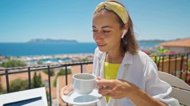 Türk tatil beldesindeki deniz manzaralı terasta oturup sabahları kahvesini yudumlayan memnun bir kadın, bilgisayarını uzaktan çalışma ve serbest konsept olarak kullanıyor. Yavaş çekim 4k