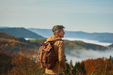 Outdoors portrait adult man with backpack admiring beautiful landscape over mountains and clouds, hiking adventurous in mountain ridge