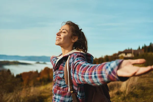 Side portrait overjoyed woman backpacker wearing a checkered jacket opening arms into the sky. girl enjoying the view on mountain hills