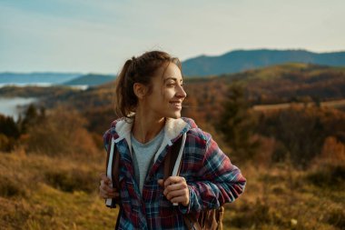 Young happy hiker woman looking around, relaxing in nature during walking backpacking by mountains range