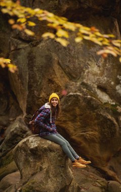 Vertical adventure image of travel hipster girl relaxing in the nature, sits on stone in old woods with mossy boulders. concept of people love for nature and planet earth