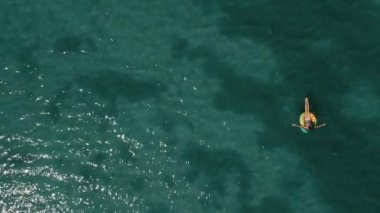 Turkuaz deniz suyunun havadan görünüşü ve yüzen sarı yüzen yüzmede yüzen kadın. Yaz mevsimi panoramik görüntüleri