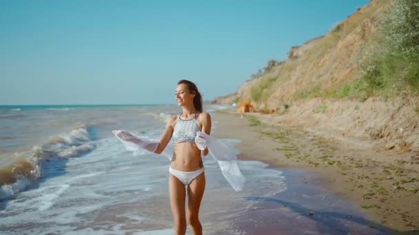 快乐快乐的苗条身材的女孩在暴风雨后享受着海滨的风浪 慢动作夏季旅游理念 身穿比基尼泳衣 身穿长袍的年轻女性在海滩上快乐地微笑 — 图库视频影像