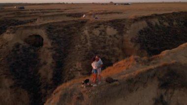 Mutlu çift kadın ve erkek tepede, gün batımında panoramik manzaralı Galli Corgi köpeğiyle dikiliyorlar. Güzel, neşeli insanlar doğada maceranın tadını çıkarıyorlar. Şarjörde ses var