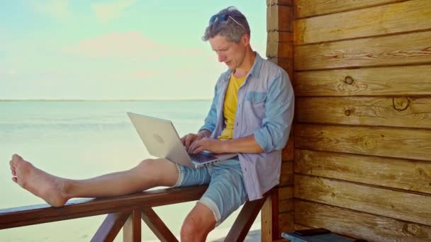 性格乐观 面带微笑的自由职业者 在海滩上用手提电脑在蓝色的海面上工作 理想的办公室工作 — 图库视频影像