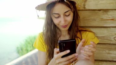 Sahilde şapkalı bir kadın dizüstü bilgisayar kullanıyor, akıllı telefon kullanıyor, internette sohbet ediyor, internette geziniyor. Teknoloji ve seyahat, tatilde online iletişim..