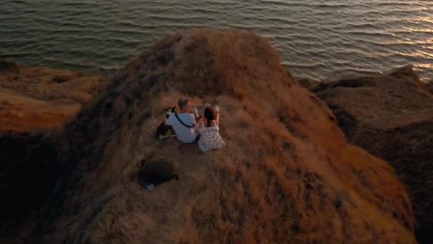 幸せなロマンチックなカップルの空中映像は 湿ったコーギー犬と日没のパノラマビューで丘の上に座っています 自然の中で冒険を楽しむ美しい喜びの人々 クリップにはノイズが — ストック動画