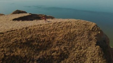 Hava manzaralı esneme egzersizleri. Fitness etrafında İHA uçuşları yapan kadın koşucu sabah egzersiz yapıyor ve deniz kıyısındaki kil tepe kanyonunda esniyor.