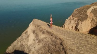 Hava manzaralı esneme egzersizleri. Fitness etrafında İHA uçuşları yapan kadın koşucu sabah egzersiz yapıyor ve deniz kıyısındaki kil tepe kanyonunda esniyor.