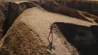 Hava manzaralı esneme egzersizleri. Fitness etrafında İHA uçuşları yapan kadın koşucu sabah egzersiz yapıyor ve deniz kıyısındaki kil tepe kanyonunda esniyor.