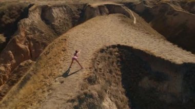 Hava manzaralı esneme egzersizleri. Fitness etrafında İHA uçuşları yapan kadın koşucu sabah egzersiz yapıyor ve deniz kıyısındaki kil tepe kanyonunda esniyor.