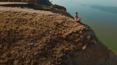 Dışarıdaki meditasyonun hava görüntüsü. Fitness etrafında İHA uçuşları yapan kadın sabahları deniz kıyısındaki kanyonun kil sırtında oturur ve egzersizlerden sonra meditasyon yapar.