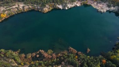 Sonbahar ormanıyla çevrili granit kıyılı bir gölün insansız hava aracı görüntüleri. Kuş bakışı görüş. Korostyshiv, Ukrayna, Avrupa. Sinematik çekim. UHD 4k video kaydı. Toprağın güzelliğini keşfedin.