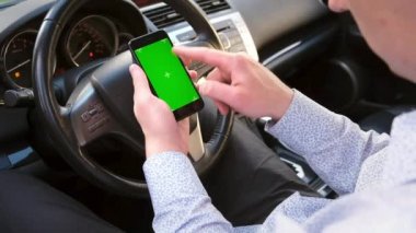 Arabada elinde cep telefonu olan genç bir adam. Chroma tuşlu dokunmatik ekran modeli. Konsept: Navigator, dağıtım, online alışveriş, internet araması.