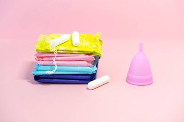Adet döngüsü. Kadınlar için kritik günlerde alternatif hijyen ve koruma araçları. Pembe arka planda hijyenik pedler, tamponlar ve silikon adet bardağı. Seçici odaklanma. Boşluğu kopyala.