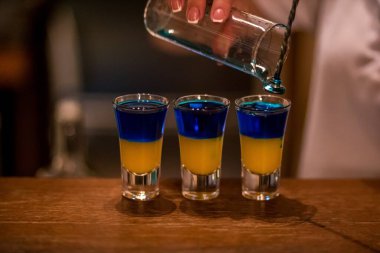 Ahşap bir masanın üzerindeki cam yığınlarında alkollü içecekler. Mavi kakao ve limon likörü..