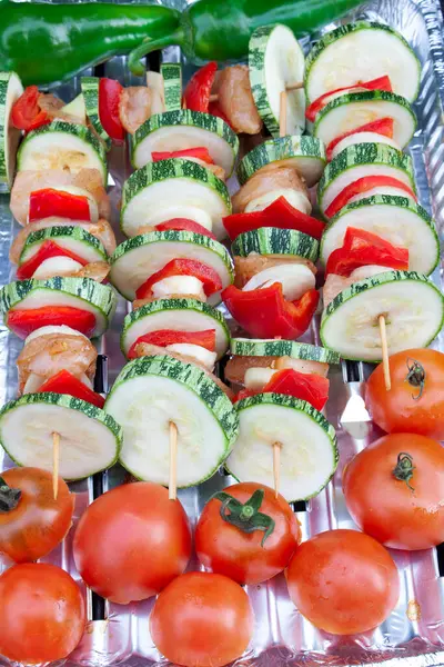 Sebzeli ızgara şişler, tavuk eti ve alüminyum tepsiye konmuş domatesler..