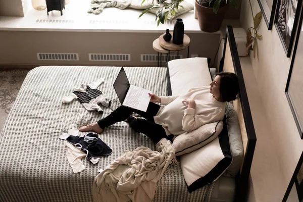 Een zwangere vrouw in een warme trui zit op bed en kijkt naar een beweging.. — Stockfoto