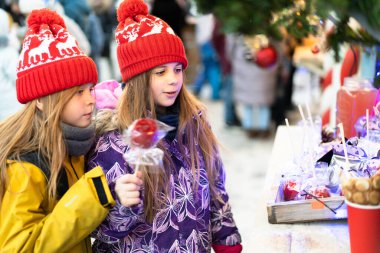 Kışın giyinmiş iki çocuk Noel pazarında ev yapımı tatlılar seçiyor..