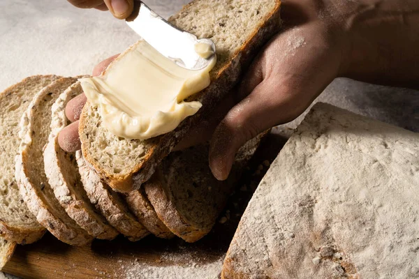 Мужские руки намазывают масло на кусок хлеба. Стоковое Изображение