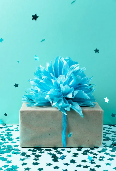 Крафт бумажная подарочная коробка с голубой лентой бант на голубом фоне с конфетти. Стоковое Фото