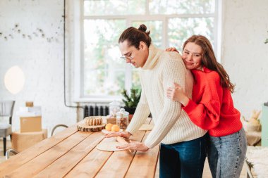 Genç mutlu çift, Noel 'de mutfakta yemek pişirirken evin içinde ışık görüntüsü yiyorlardı.