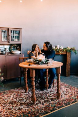 Noel kutlaması çifti evde, masada Xmas dekorasyonlarıyla oturuyor. İnsanlar içeride.