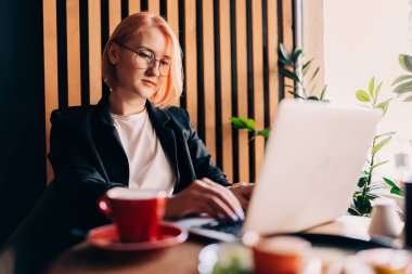 Genç iş kadını kafede kahve içiyor ve dizüstü bilgisayarda çalışıyor.