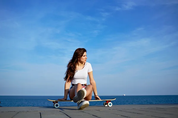 Menina bonita sentada no longboard olhando para longe — Fotografia de Stock