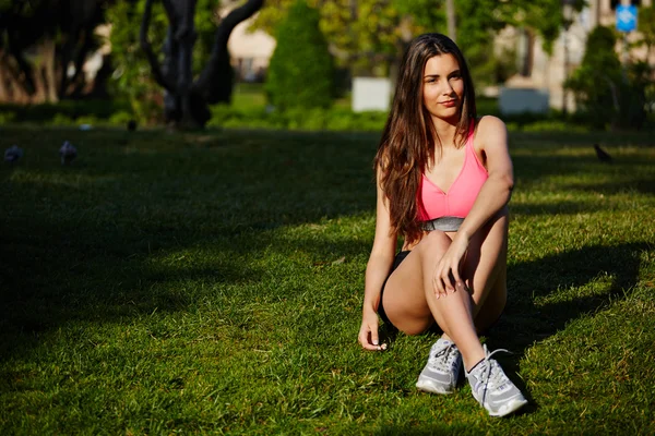 Спортивная девушка сидела на траве и отдыхала после пробежки в красивом парке — стоковое фото